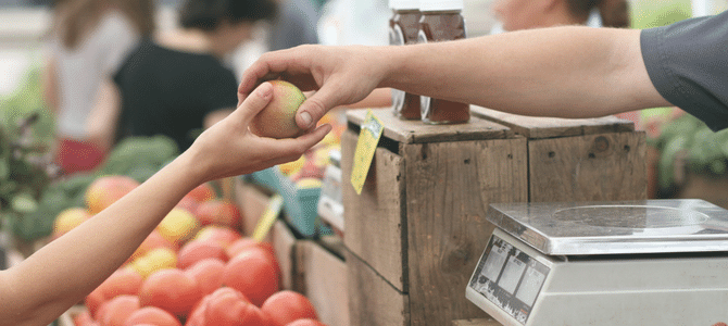 A person purchasing an apple at a farmers market in a small town